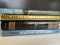 Side view of the four stacked large art books showing titles and authors on spines.