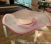 Angle view of free-form frosted white and pink glass art bowl on glass table, showing shape and texture