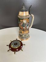 Photo showing both the brass barometer in ship's wheel wooden case and the sculpted lidded beer stein together.