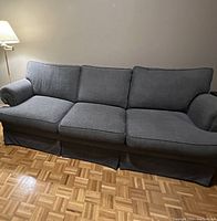 Full view of the charcoal grey chenille fabric couch showing three seat cushions and three back cushions with rolled arms and skirted base.