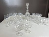 Crystal decanter with stopper and assortment of stemware including red wine, white wine, cordial, and champagne glasses on a white round table.