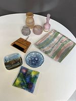 Full lot of decorative accessories on white table showing ceramic platter, bubble glass bowl, multicoloured glass dish, wooden mini brush and dustpan, acrylic mini-plate with photo image, and assorted glass vessels