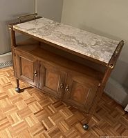 Front angle view showing closed cabinet doors, marble top, wood shelf and brass castors.