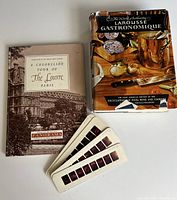 Larousse Gastronomique culinary book with dust jacket and Louvre tour book with color slides laid flat on a surface