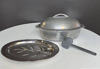 Photo showing the heavy metal roaster with lid, silver-plated Viking meat platter, and meat tenderizer on black background.