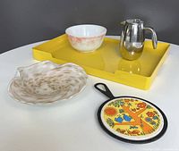 Overview of the full set arranged on a table including red and white mixing bowls, steel French press, yellow tray, decorative trivet, and art glass bowl