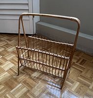Single photo showing a natural bamboo and rattan magazine rack on a parquet floor near a vent and door.