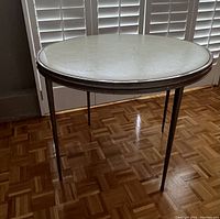 Full view of the round metal folding table set up showing the off-white padded top and metal legs.