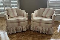 Pair of Mid-Century Modern style tub chairs with peach striped moire fabric upholstery and matching pillows, sitting on parquet floor near window with shutters.