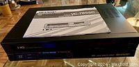 Front view of Sharp VC-7855C VCR with manual placed on top.