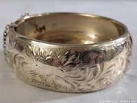 Front angle showing carved floral and scroll engravings on thick silver cuff bracelet.