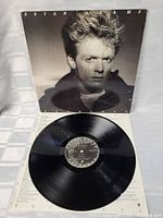 Black and white album cover of Bryan Adams with the vinyl record placed on top, showing the vinyl in very good condition with the album insert beneath.