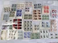 Top view of multiple blocks of four Canadian postage stamps laid out, showing diverse designs, colors, eras mid-20th Century.