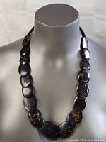 Front view of the vintage necklace displayed on a bust, showing dark oval beads with a golden speckled pattern.