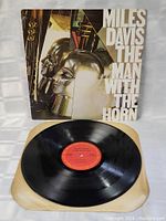 Opened vinyl record showing black disc with red label and album cover with abstract horned head artwork and title text.