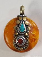Front close-up showing the round orange coral base with silver, gold accents, turquoise teardrop stone, and red coral circular stone.
