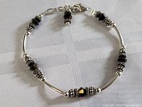 Full view of sterling silver bracelet showing alternating black stones with silver decorative beads and polished tube links on light fabric background.