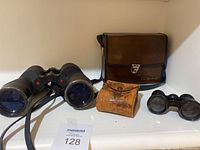 Two pairs of binoculars and two cases including a large Bushnell case on shelf