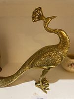 Side view of brass peacock statue showing detailed floral engravings and shape
