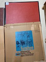 Photo of the original cardboard box packaging for the card table featuring brand name 'Cooey' and line 'Furniture designed for modern living'.