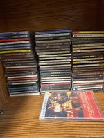 Multiple stacks showing a large variety of music CDs arranged on a wooden shelf.