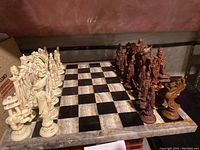 Chessboard with light and dark carved chess pieces arranged, showing detailed carved designs on pieces and marble board pattern.