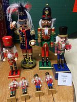 Full view of nine Christmas nutcracker figures displayed upright on wooden surface, showing various sizes, colors, and styles.