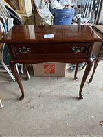 Full front view of the console table showcasing the wood finish, drawer, and cabriole legs.