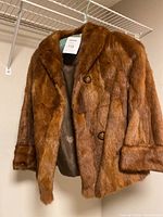 Front view of brown short fur jacket on hanger showing soft fur texture and button closure.