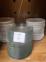 Stacks of white ceramic plates and textured clear glass plates on wooden shelving.