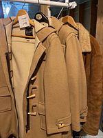 Three men's jackets hanging on a metal rack showing wool and sheepskin materials