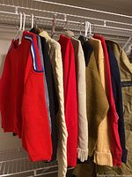 Side view of 8 men's shirts and sweaters on hangers in closet, showing variety of colors and styles.