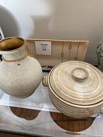 Pottery vase, covered dish, and small platter displayed together on glass surface with wooden floor visible.