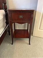 Full front view of dark wood night stand with one drawer and lower shelf, showing carved details on sides.