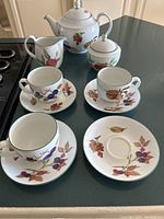 Full view of tea set on surface showing cups, saucers, teapot, creamer, and sugar bowl with fruit pattern