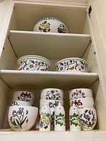 All ceramic bowls and three shakers arranged on three shelves inside a cabinet