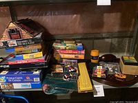 Wide shot of all puzzle boxes stacked, and various game items including cribbage board and coins, and a small orange toy vehicle.