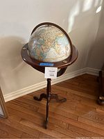 Full view of a standing globe mounted on a wooden tripod stand with decorative brass accents, 37 inches tall.