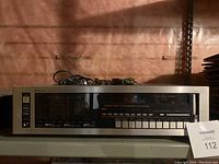 Front view of Sherwood AM/FM stereo receiver showing main display with frequency indicators and control buttons, placed on a shelf with insulation background.