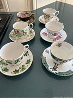 Overview of six different teacup and saucer sets showing variety of floral and plaid patterns with gold trimming.