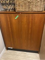 Closed teak cabinet showing two front doors with vertical wood grain and a small white chip on the bottom left corner.