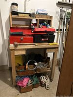 Photo of wooden workbench with red metal toolboxes stacked, black Craftsman plastic toolbox, hand tools, brushes, and other supplies on shelves and on bench surface.