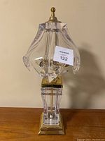 Front view of the lamp showing clear glass drip style shade, brass finial, and pedestal base.