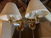 Pair of brass wall sconce lamps with cream feather pleat shades lying inside a cardboard box.
