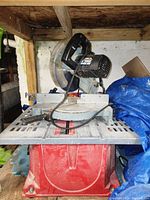 Front view of the Delta 10-inch power miter saw showing black motor housing, silver blade guard, and red base with dust and dirt.