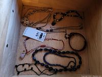 Overview of assorted necklaces in a wooden drawer including amethyst and quartz bead necklaces plus others in black and gold-tone chains.
