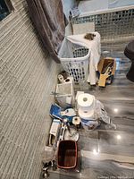 Overall lot details showing bathroom and household items including basket, toilet paper, hook, irons, and accessories on tiled floor.