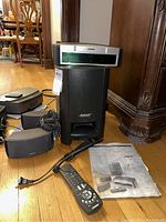 Overall shot of Bose 321 system including subwoofer, satellite speakers, remote, manual on hardwood floor.