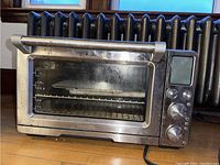 Front view of the stainless steel Breville toaster oven showing glass door with measurement markings and ventilation on top.