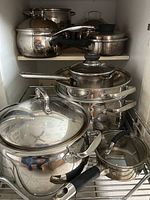Photo of assorted stainless steel pots and saucepans with lids, various sizes, some with plastic handles.